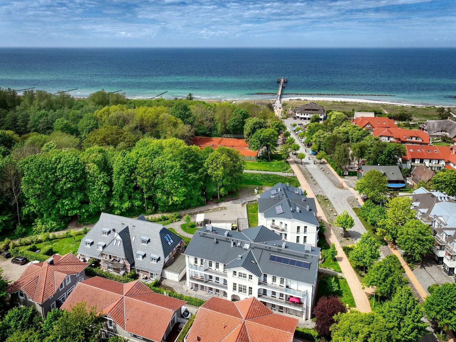 Aerial view of coastal village with houses, trees, and ocean in background.