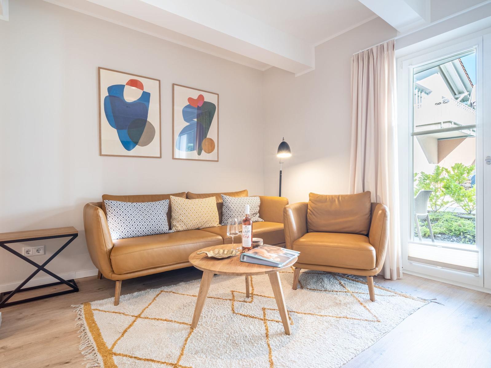 Ein Wohnzimmer mit braunem Sofa, Sessel und Holztisch. An der Wand hängen zwei abstrakte Bilder.
