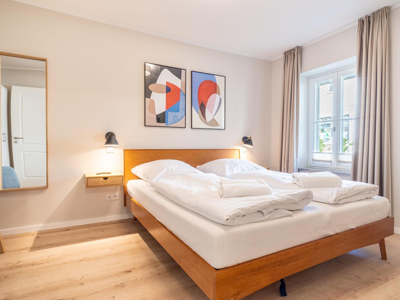 Schlafzimmer mit Doppelbett, Holzfußboden und Fenster mit Vorhängen.
