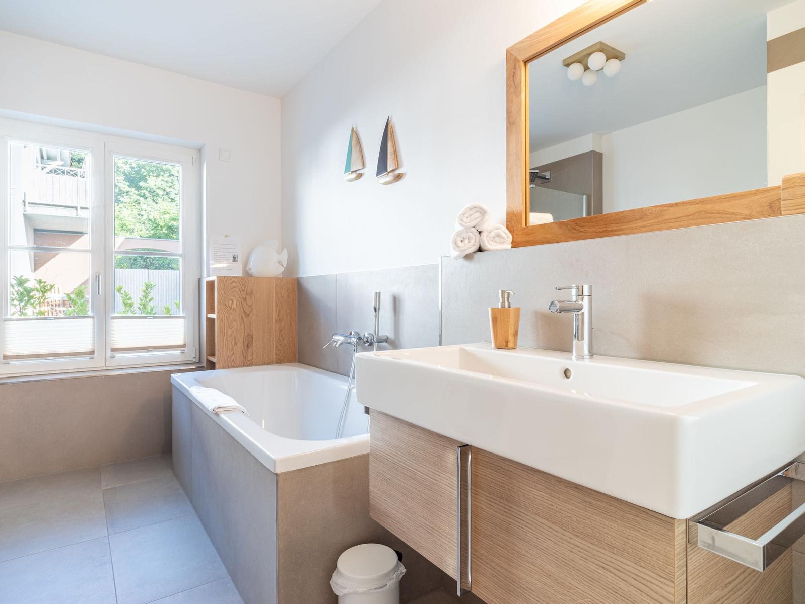 Badezimmer mit Badewanne, Waschbecken und Fenster mit Blick nach außen.
