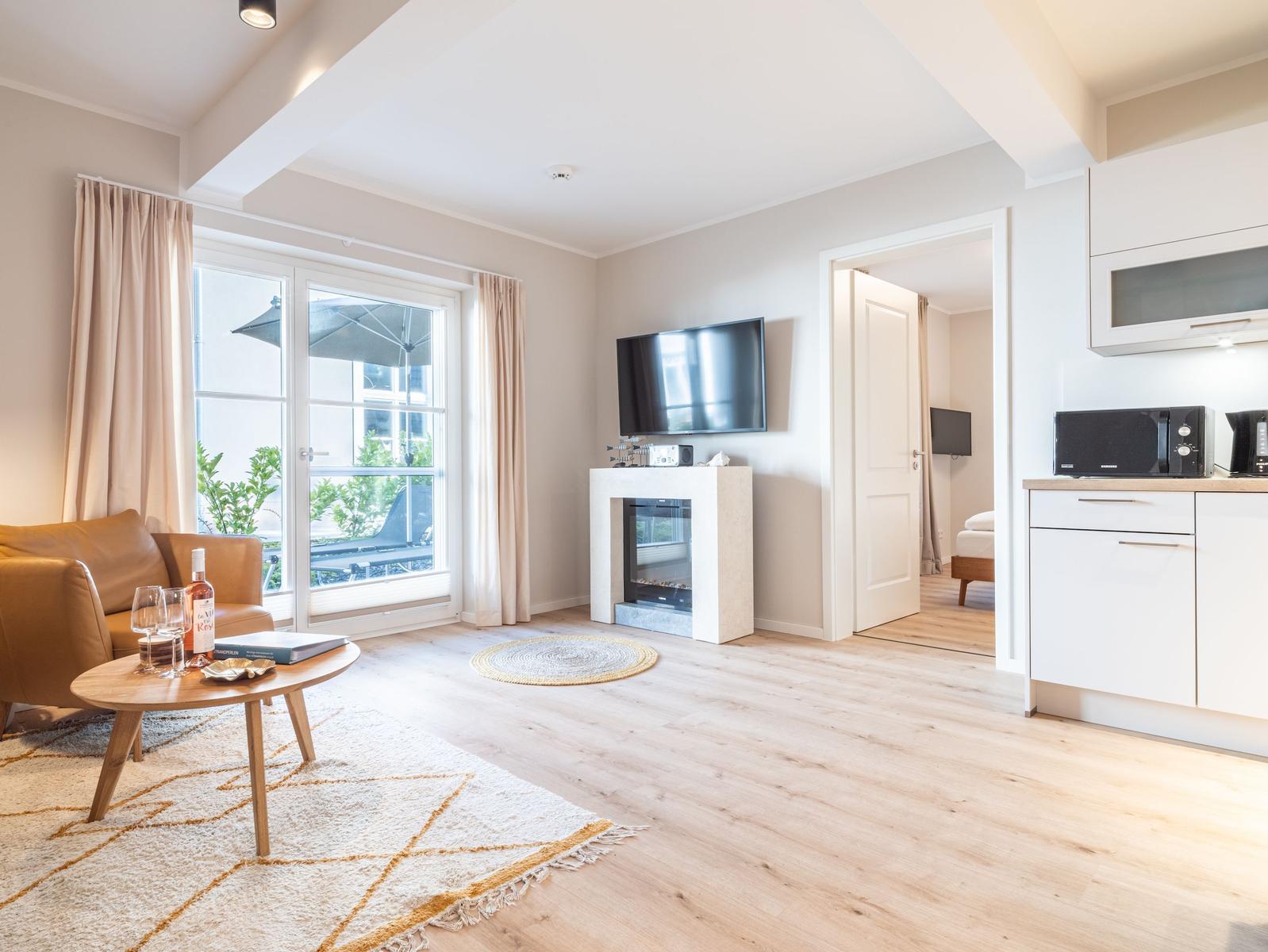 Wohnzimmer mit Sofa, Fernseher und Kamin. Durchgang zur Schlafzimmer. Küche mit Mikrowelle.