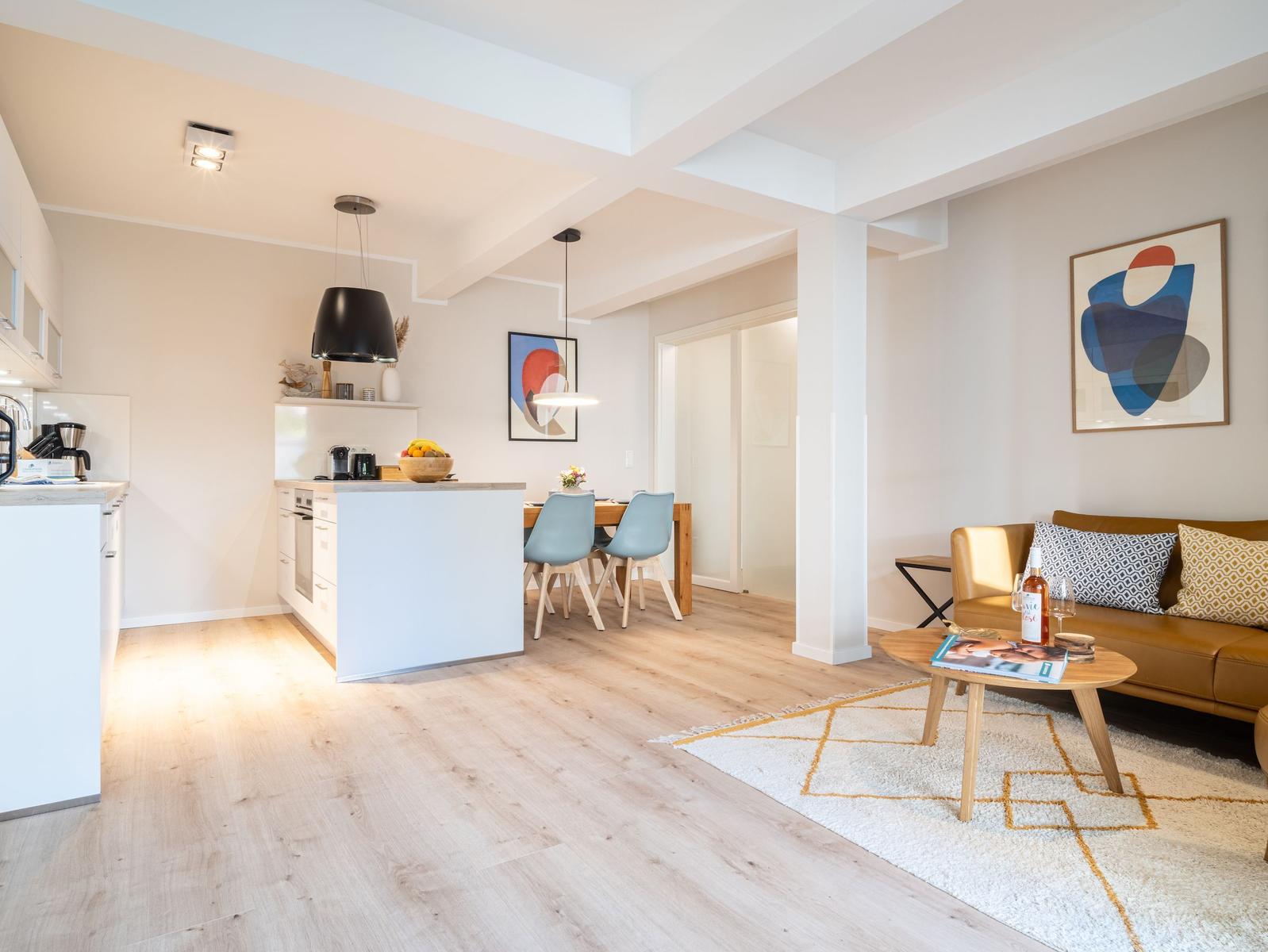 Wohn- und Essbereich mit Küche, Sofa und Tisch. Holzboden und moderne Einrichtung.
