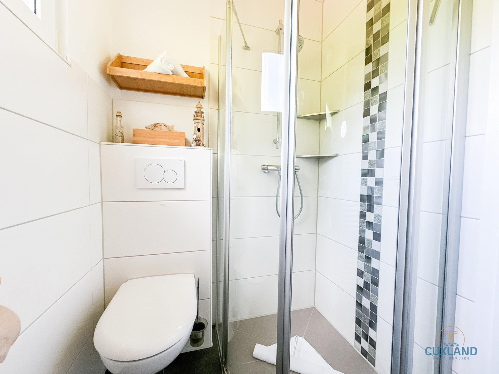 Bad mit Dusche, Toilette und Holzregal an der Wand.