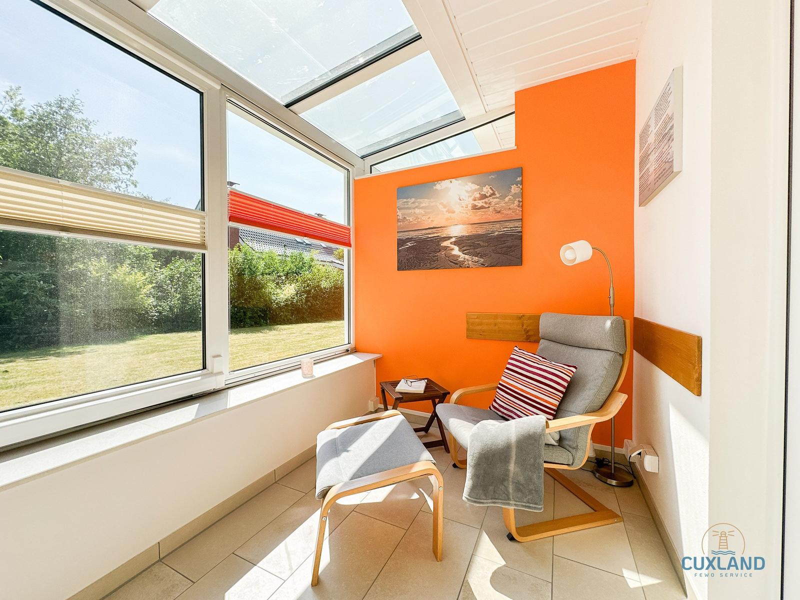 Raum mit Sitzgelegenheit, Fenster und orangefarbener Wand. Sonnenlicht fällt durch Glasdach.