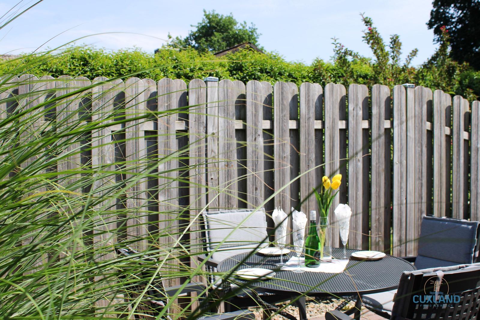 Garten mit Tisch, Stühlen und gelben Tulpen hinter Holzzaun.
