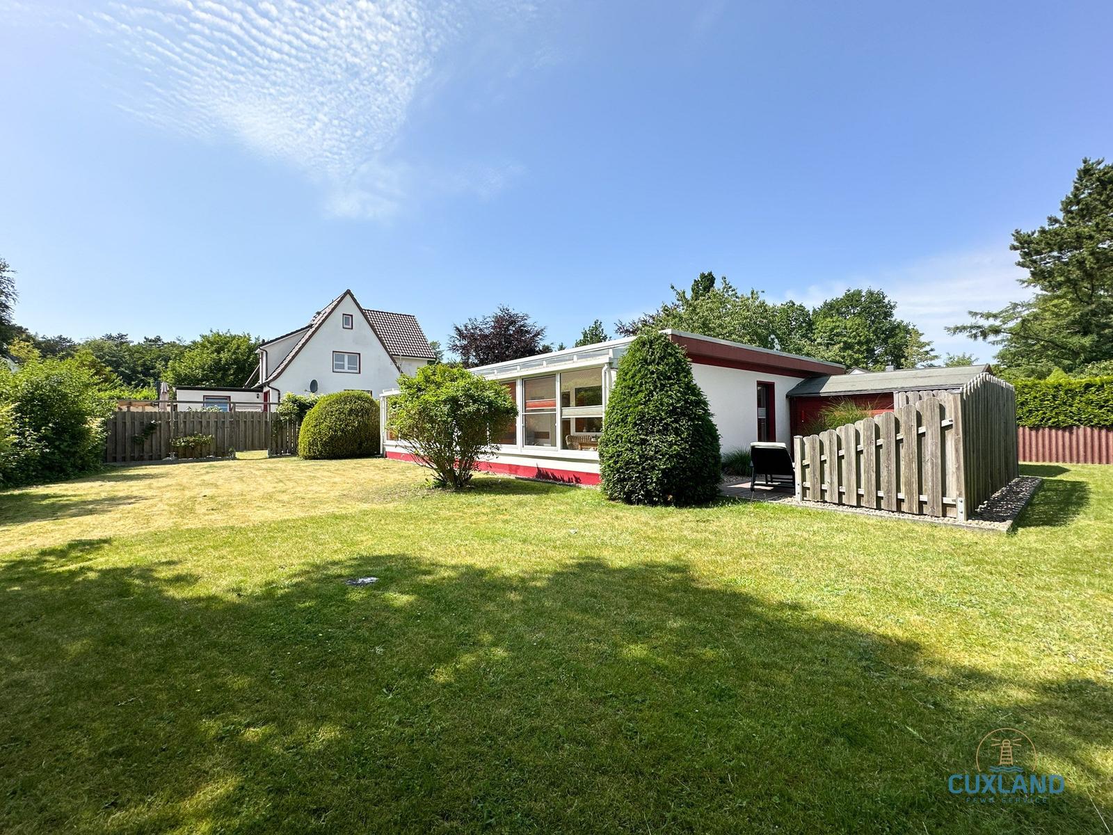 Wohnhaus mit Garten, Holzzaun und Bäumen unter blauem Himmel.