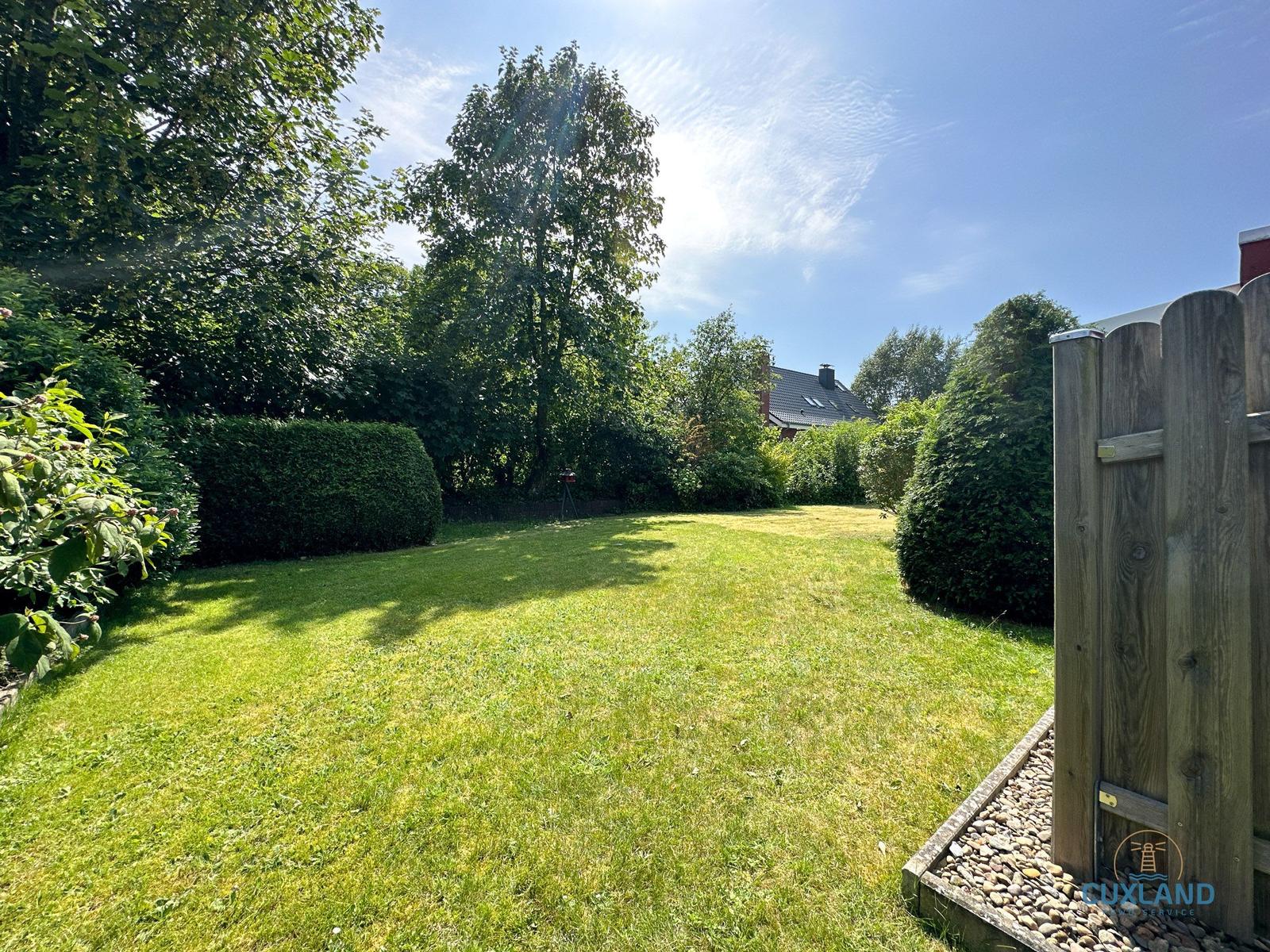 Grüner Garten mit Holzzaun und Bäumen unter blauem Himmel.