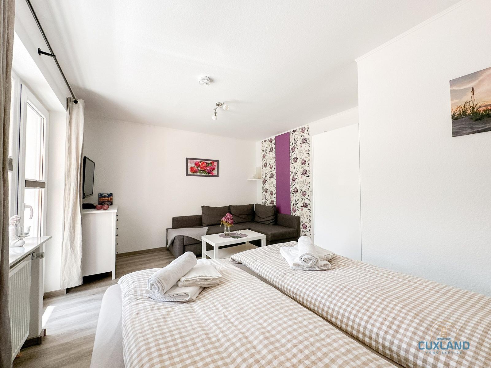 Zwei Betten mit Handtüchern, Sofa, TV und Fenster im Zimmer.