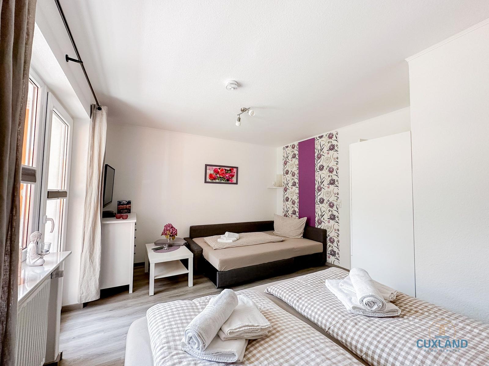 Zimmer mit zwei Betten, Sofa, Fernseher und Fenster.