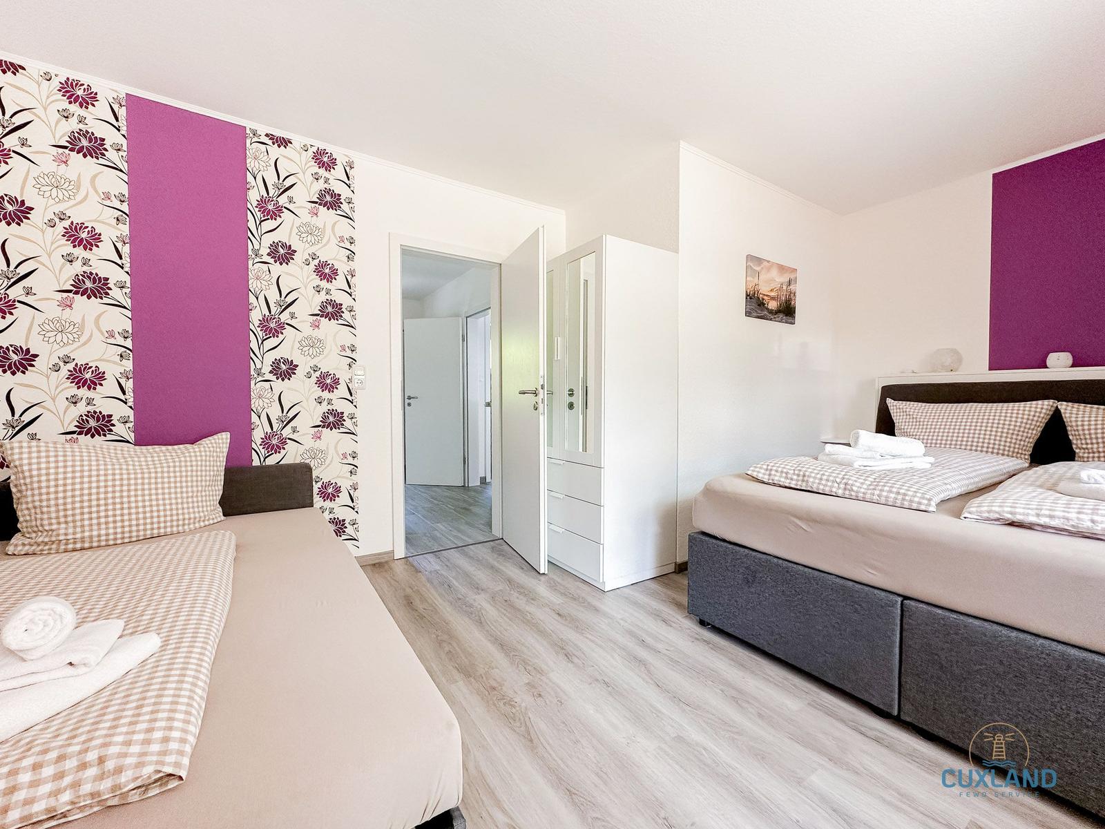 Schlafzimmer mit zwei Betten, Kleiderschrank und floraler Wandtapete.