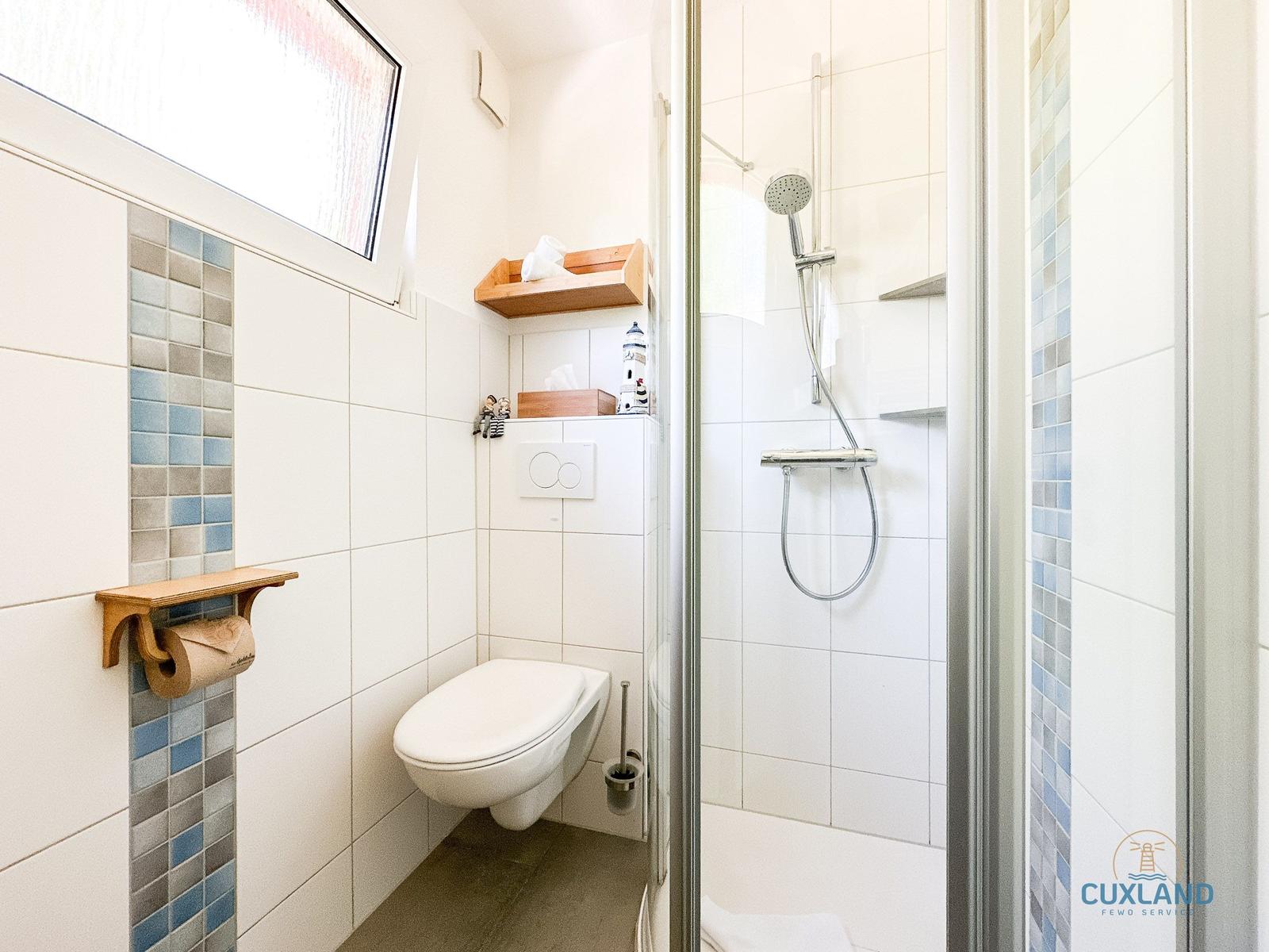 Badezimmer mit Dusche, Toilette und Holzregalen an den Wänden.