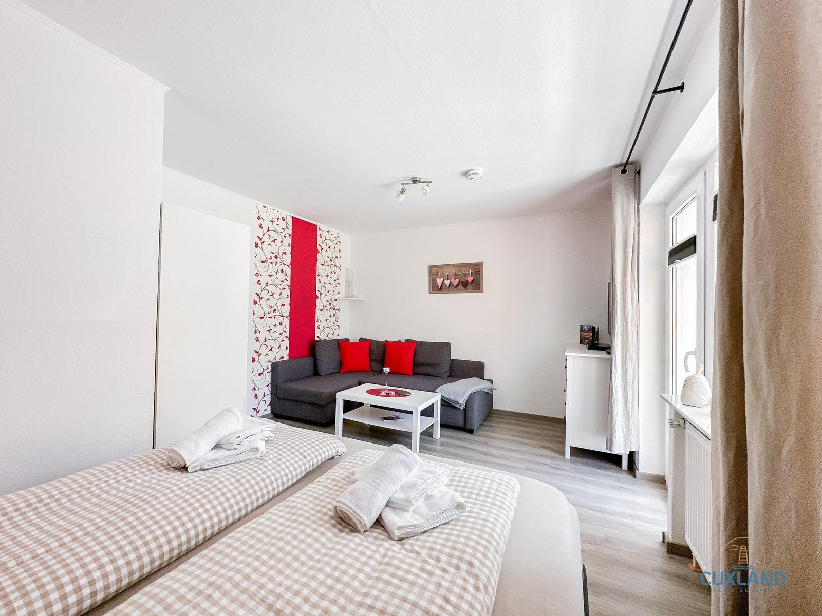 Zimmer mit Schlafbereich und Sitzgelegenheit. Wand mit Muster und roter Akzentfläche.