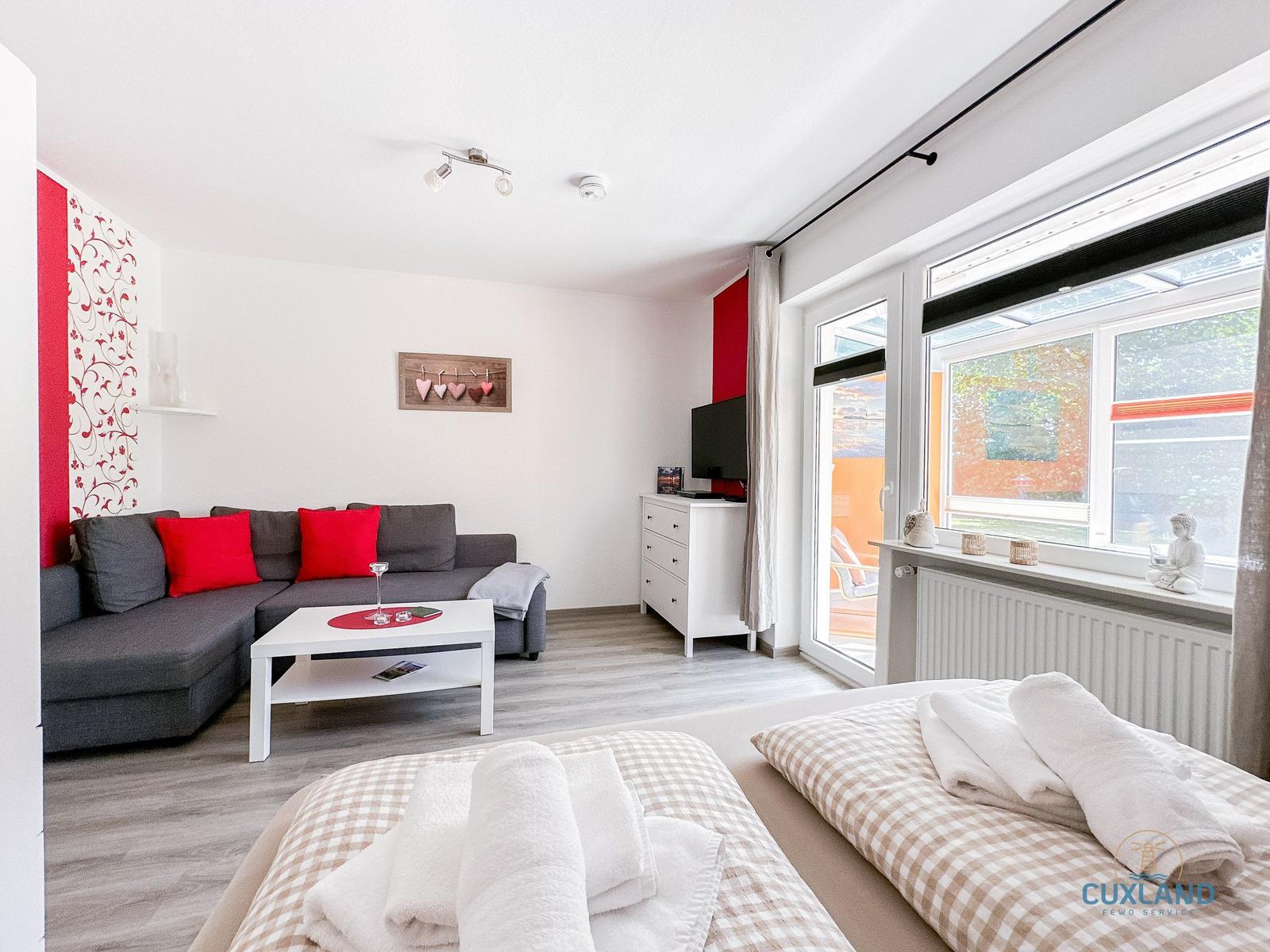 Wohnzimmer mit Sofa, TV und Schlafbereich mit Bett und Handtüchern.