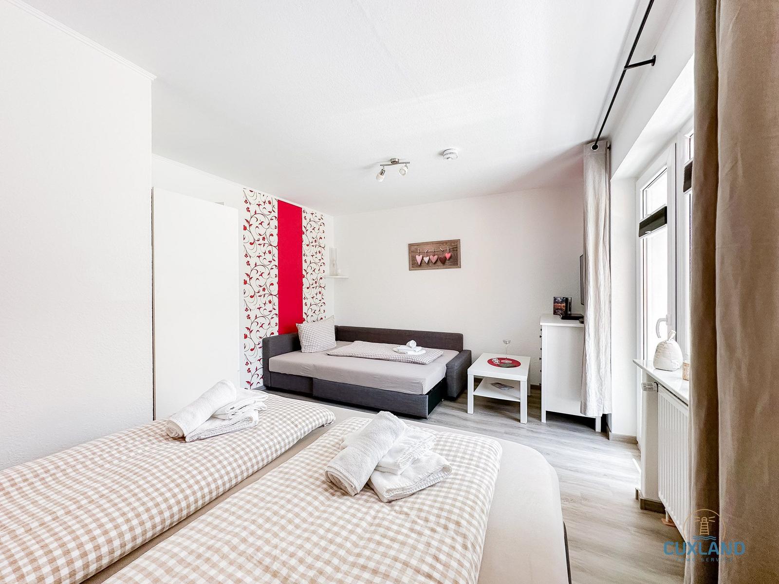 Zimmer mit zwei Betten, Sofa, Tisch und Fenster mit Vorhängen.