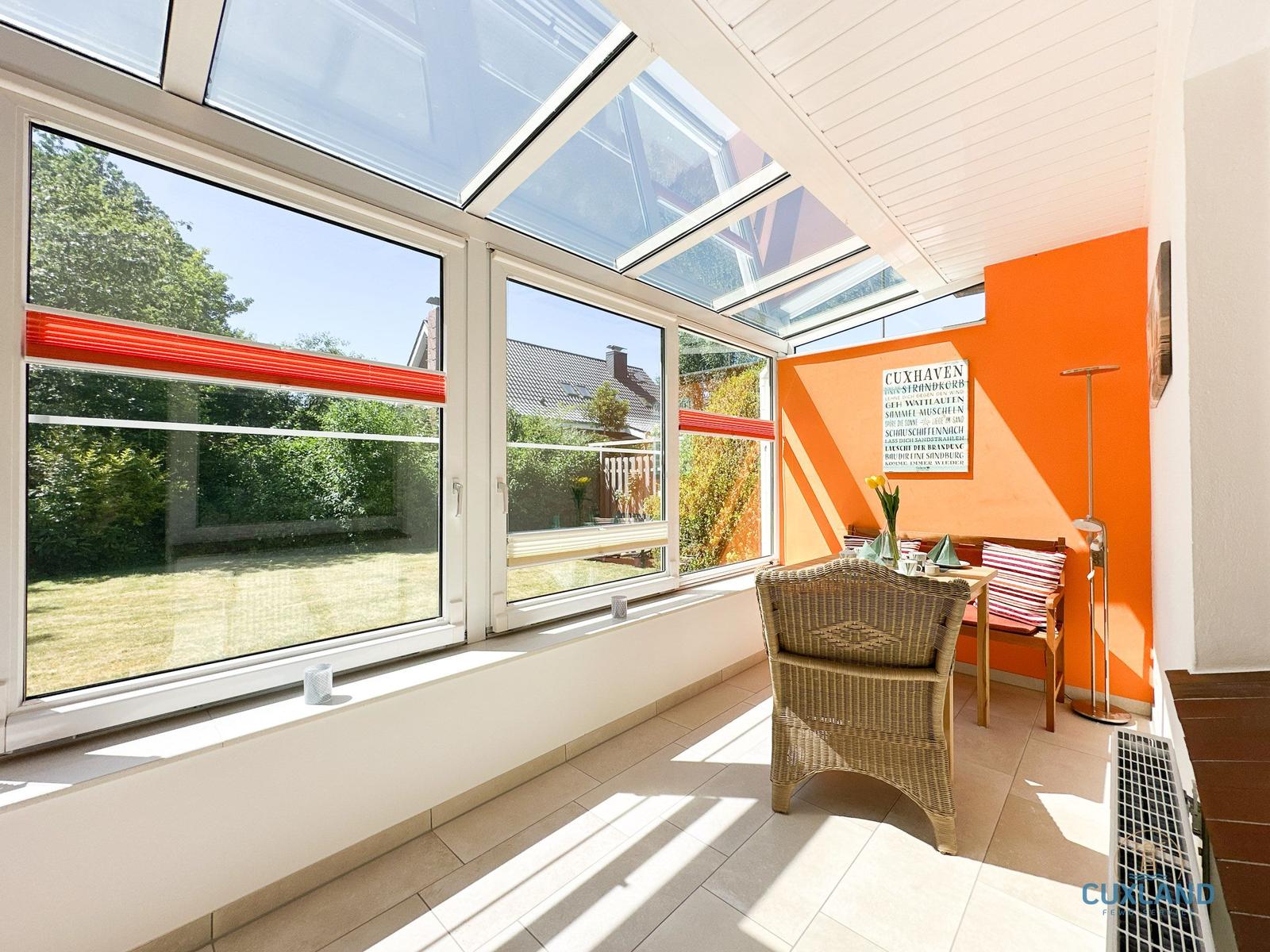 Sonnige Veranda mit orangefarbener Wand, Sitzgelegenheit und Blick auf Garten.