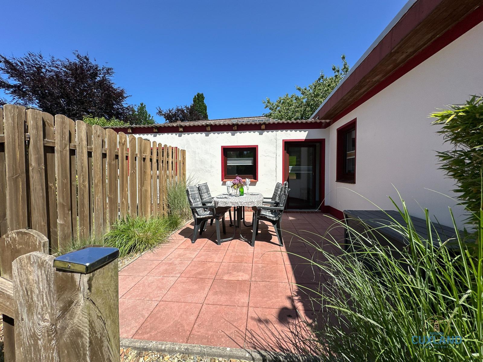 Terrasse mit Tisch und Stühlen, umgeben von Holzzaun und Grünflächen.