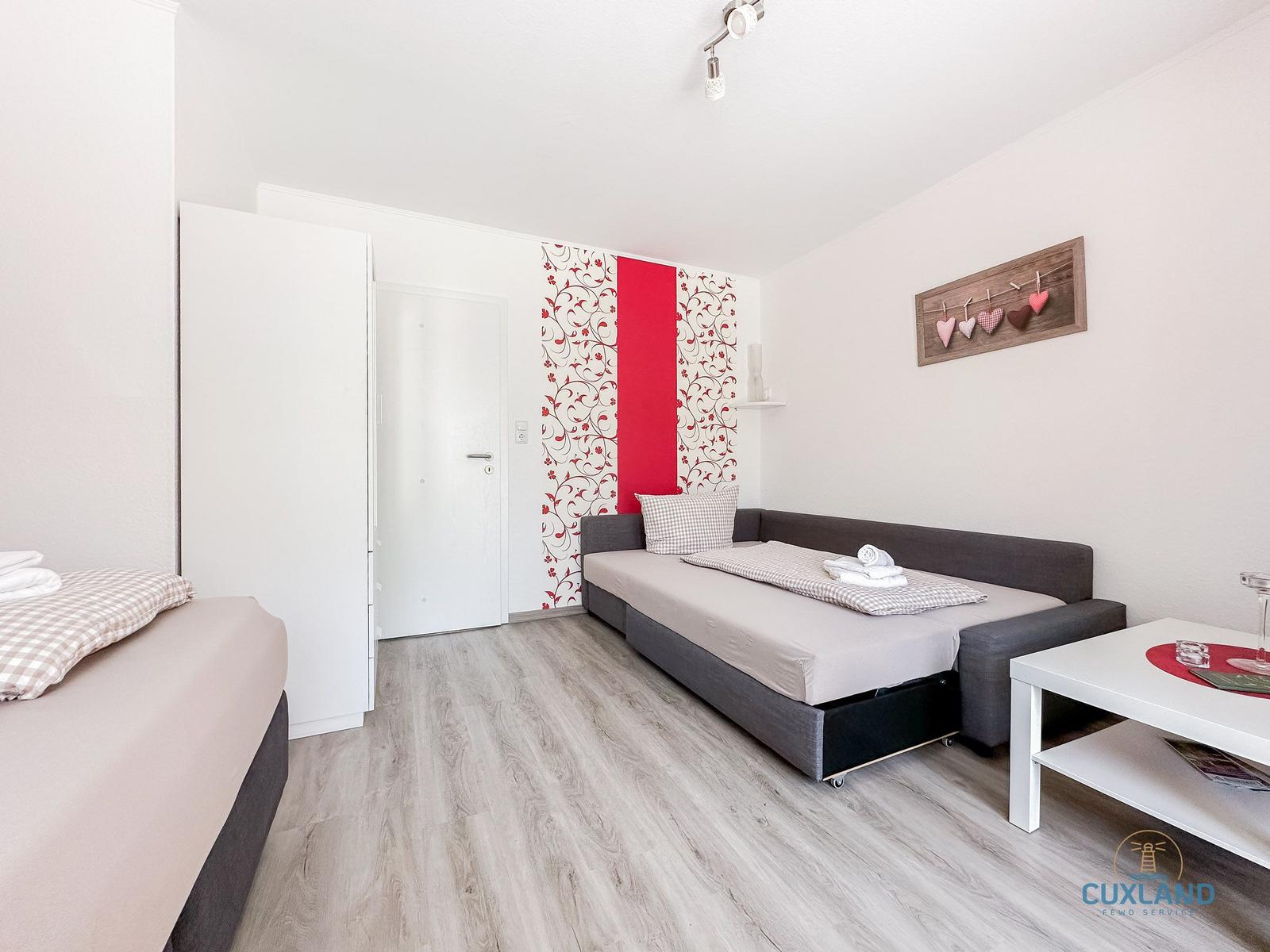 Zimmer mit Schlafcouch, Schrank und dekorativer Wandverkleidung.