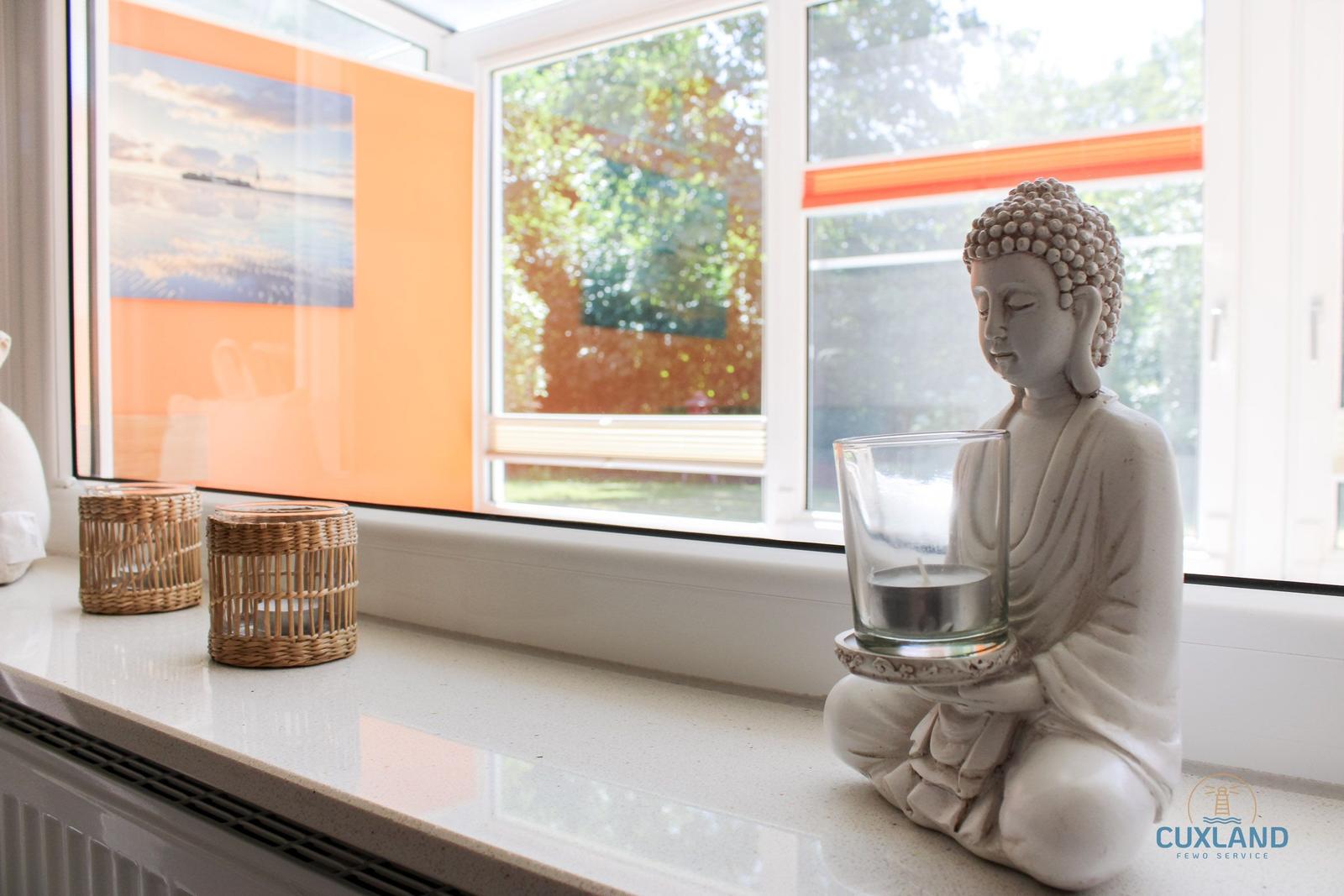 Buddha-Statue auf Fensterbank mit Kerzenhaltern und Blick auf Garten.