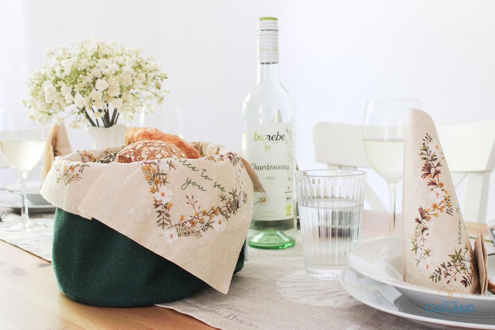 Tisch gedeckt mit Brot, Wein, Blumen und Geschirr.