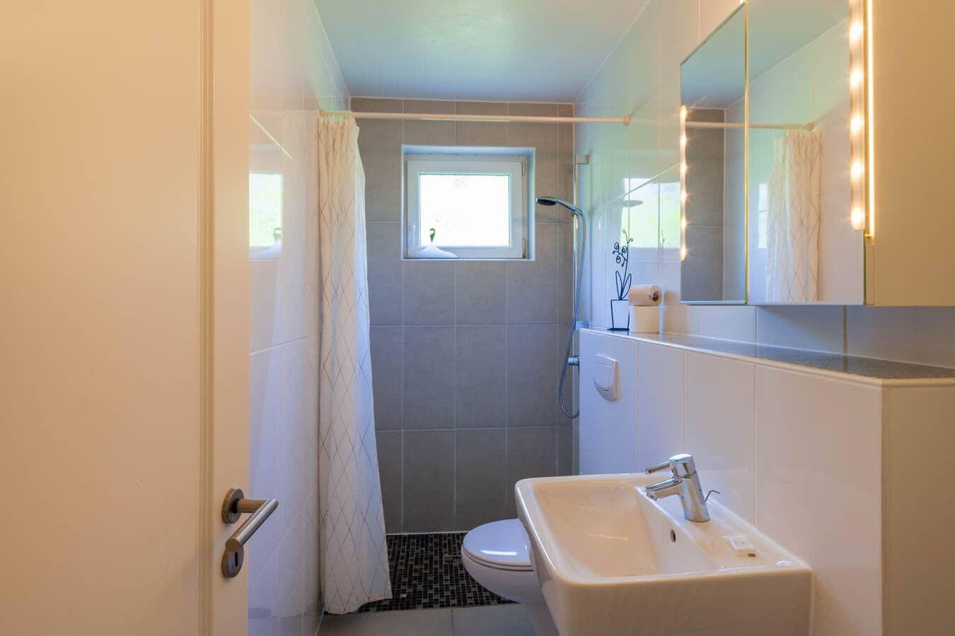 Badezimmer mit Dusche, Toilette und Waschbecken. Fenster sorgt für Tageslicht.