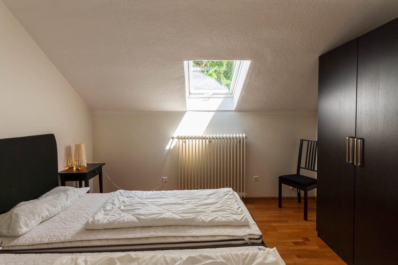 Schlafzimmer mit Dachfenster, Bett, Kleiderschrank und Stuhl.