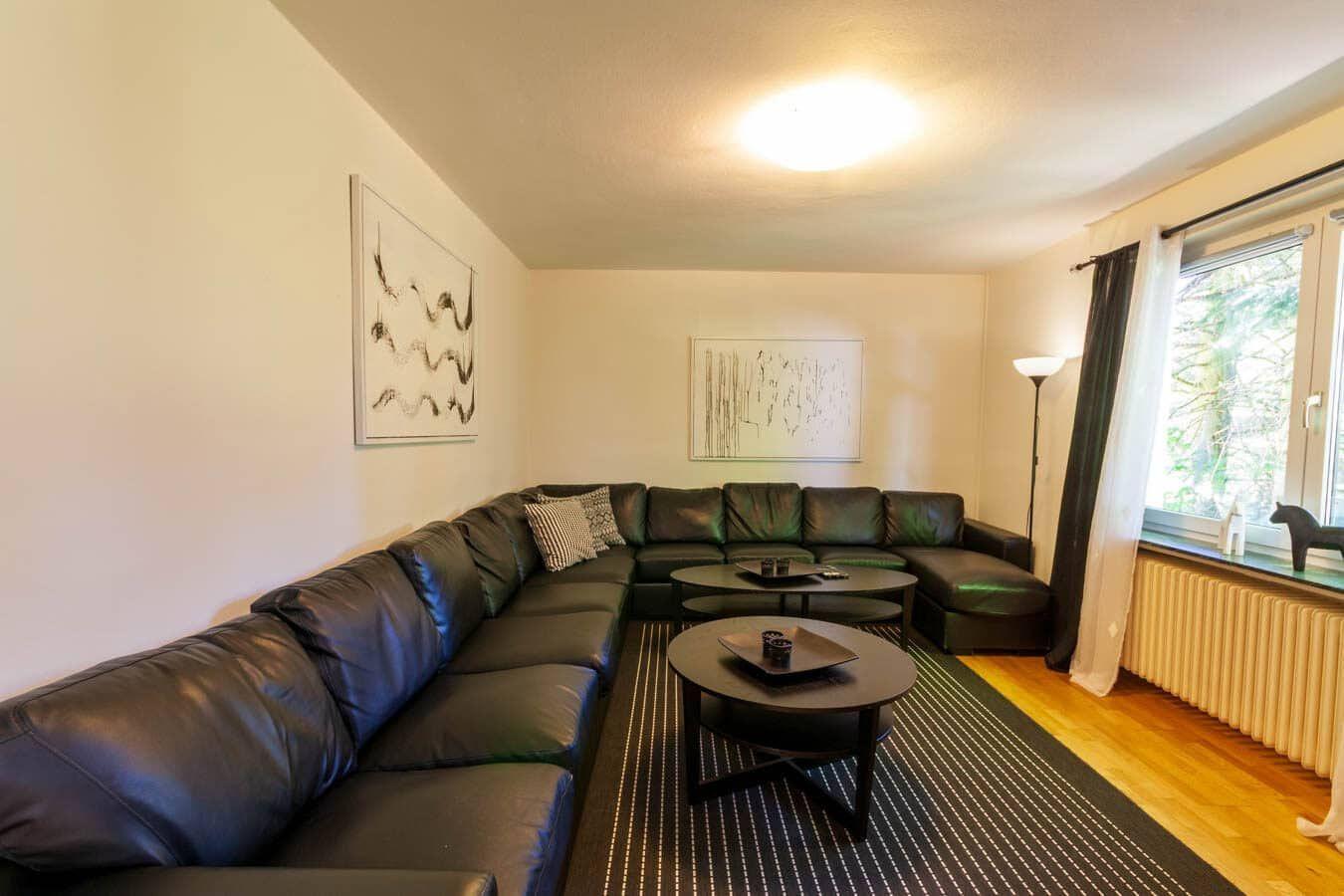 Wohnzimmer mit L-Förmigem Sofa, zwei runden Tischen und Fenster mit Blick auf Bäume.