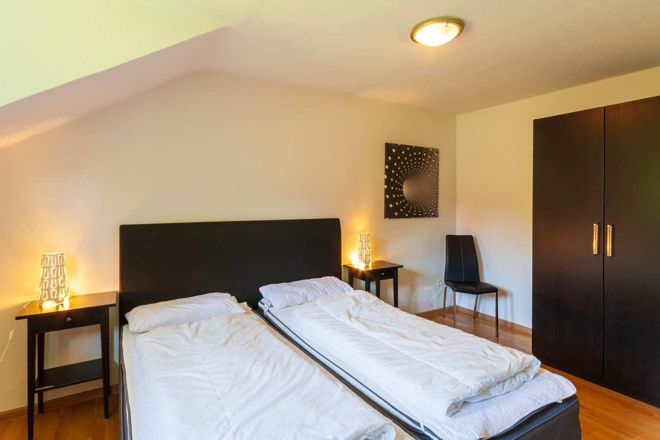 Zimmer mit zwei Betten, Schrank und Nachttisch mit Lampe.