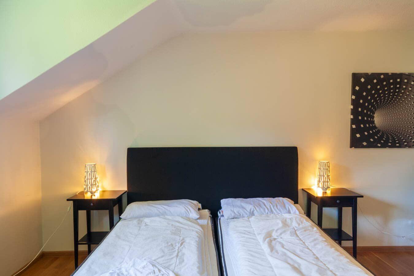 Zwei Betten mit weißen Bettwäsche, schwarze Nachttische mit Lampen, schräges Dach und Wandbild.