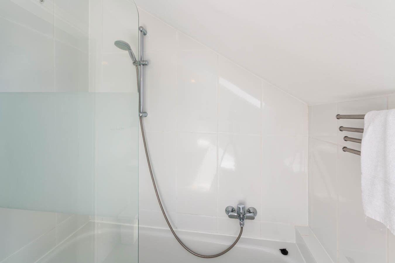 Dusche mit Duschbrause und Handbrause in Badewanne mit Glaswand und Handtuchhalter.