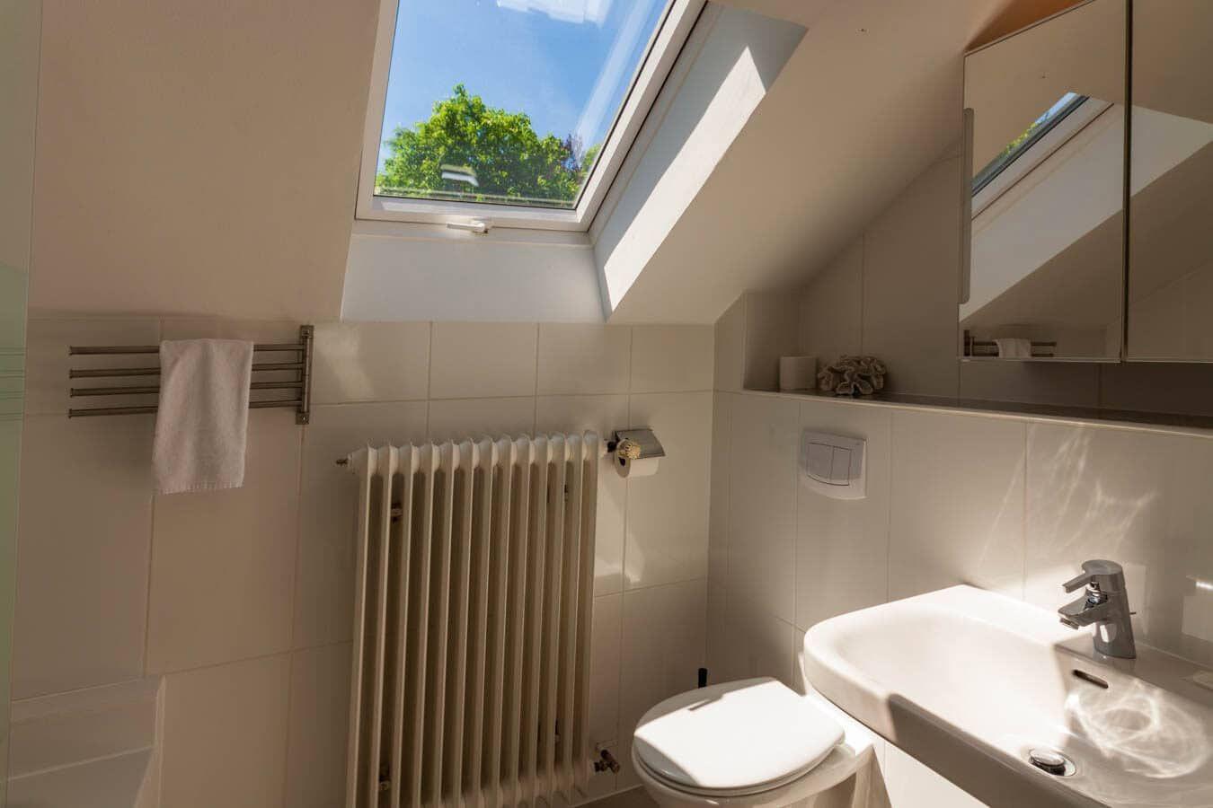 Badezimmer mit Dachfenster, Waschbecken, Toilette und Heizkörper.