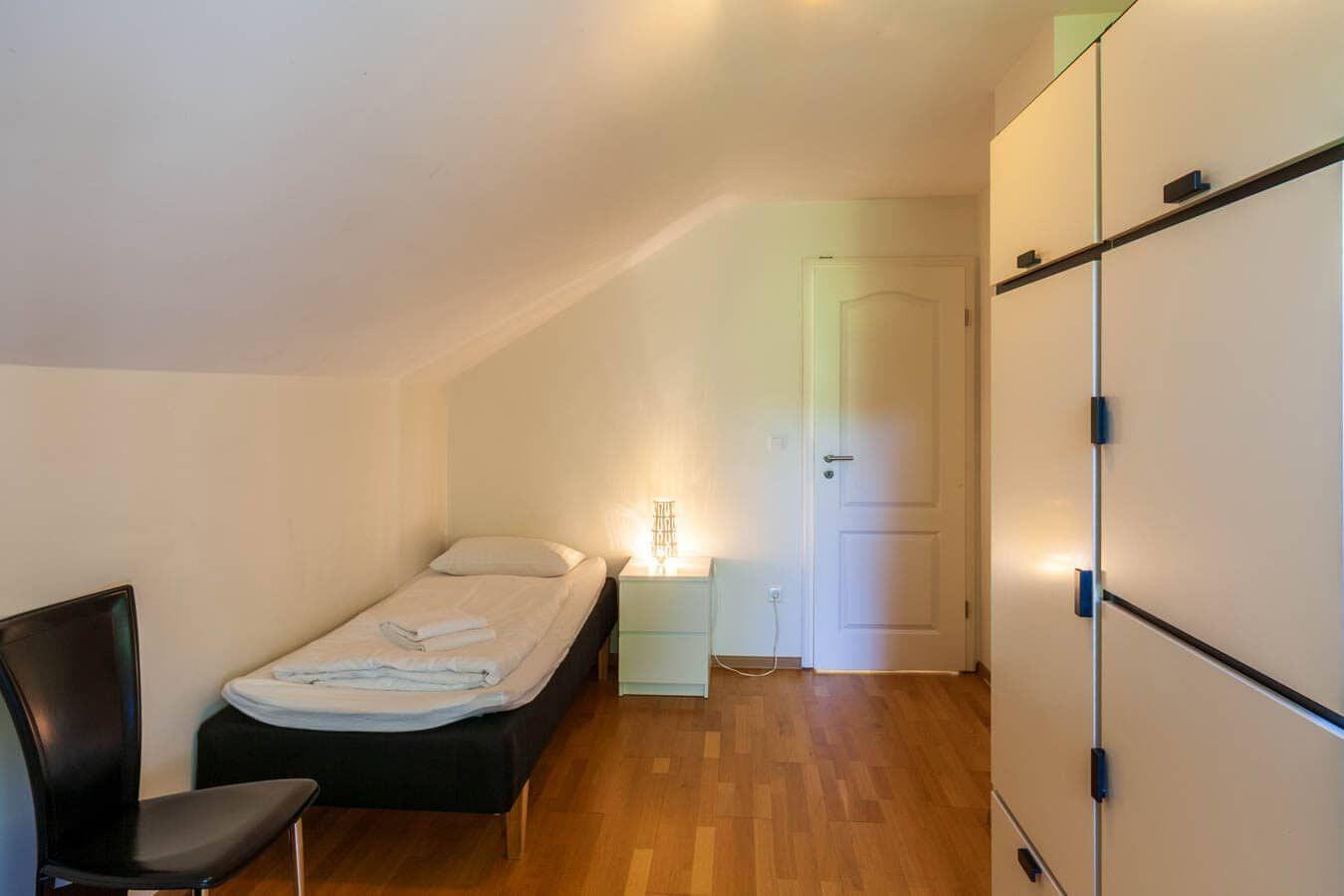 Schlafzimmer mit Einzelbett, Nachttisch und Kleiderschrank. Holzboden und schräges Dach.