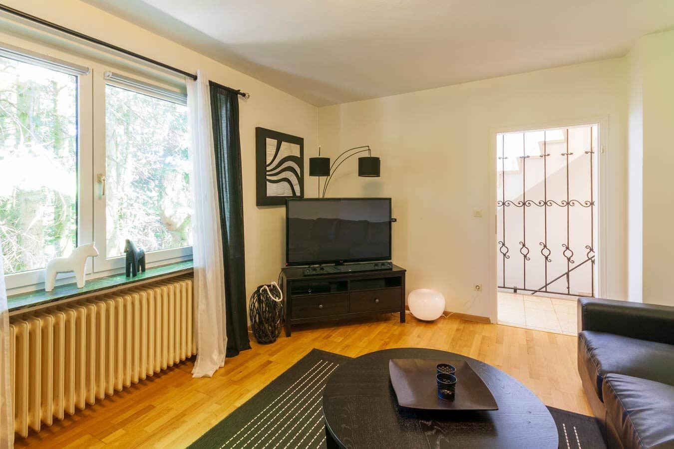 Wohnzimmer mit Holzboden, Sofa, Fernseher und Fenster mit Blick auf Wald.