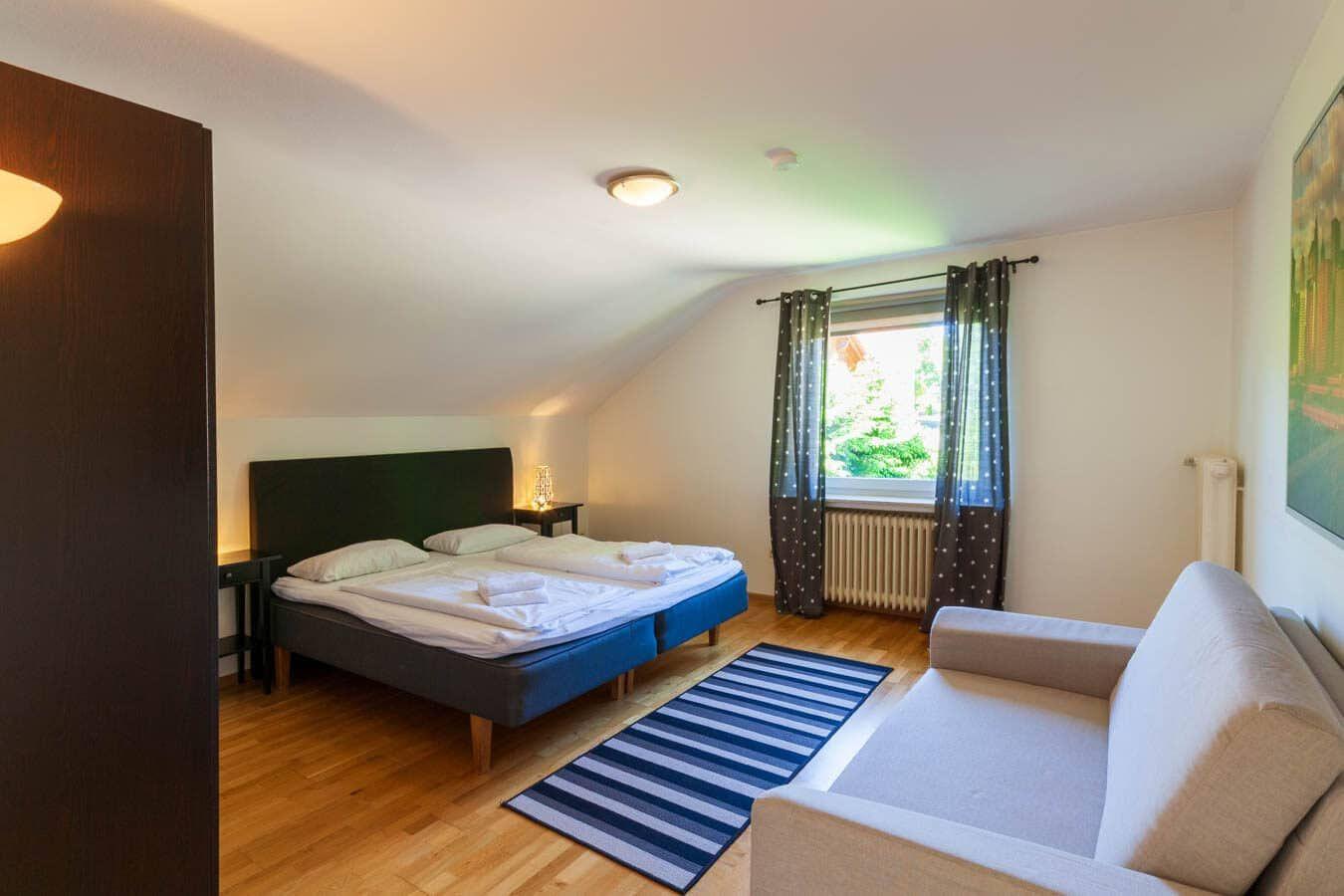 Schlafzimmer mit Doppelbett, Sofa und Fenster mit Blick nach draußen.
