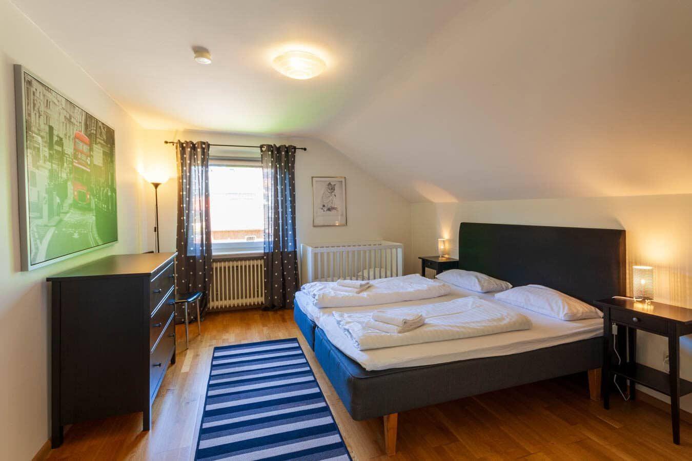 Schlafzimmer mit Doppelbett, Kleiderschrank und Fenster mit Vorhängen.