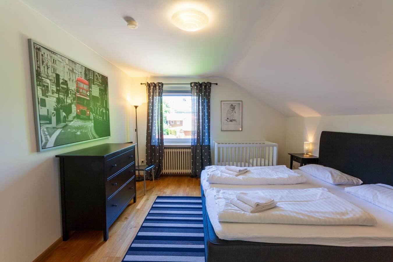 Schlafzimmer mit Doppelbett, Babybett, Schrank und Fenster mit Vorhängen.