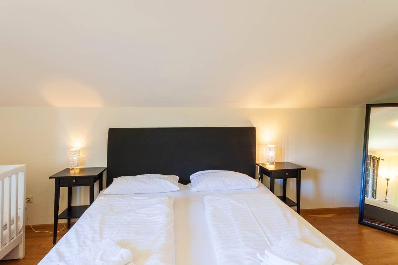 Schlafzimmer mit Doppelbett, zwei Nachttischen und einem Kinderbett.