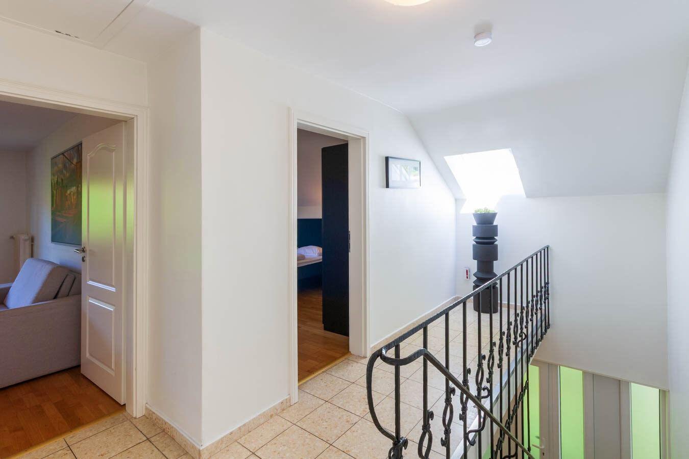 Flur mit Treppe, Tür zu Schlafzimmer und Wohnzimmer. Dachfenster und schwarze Pflanze.