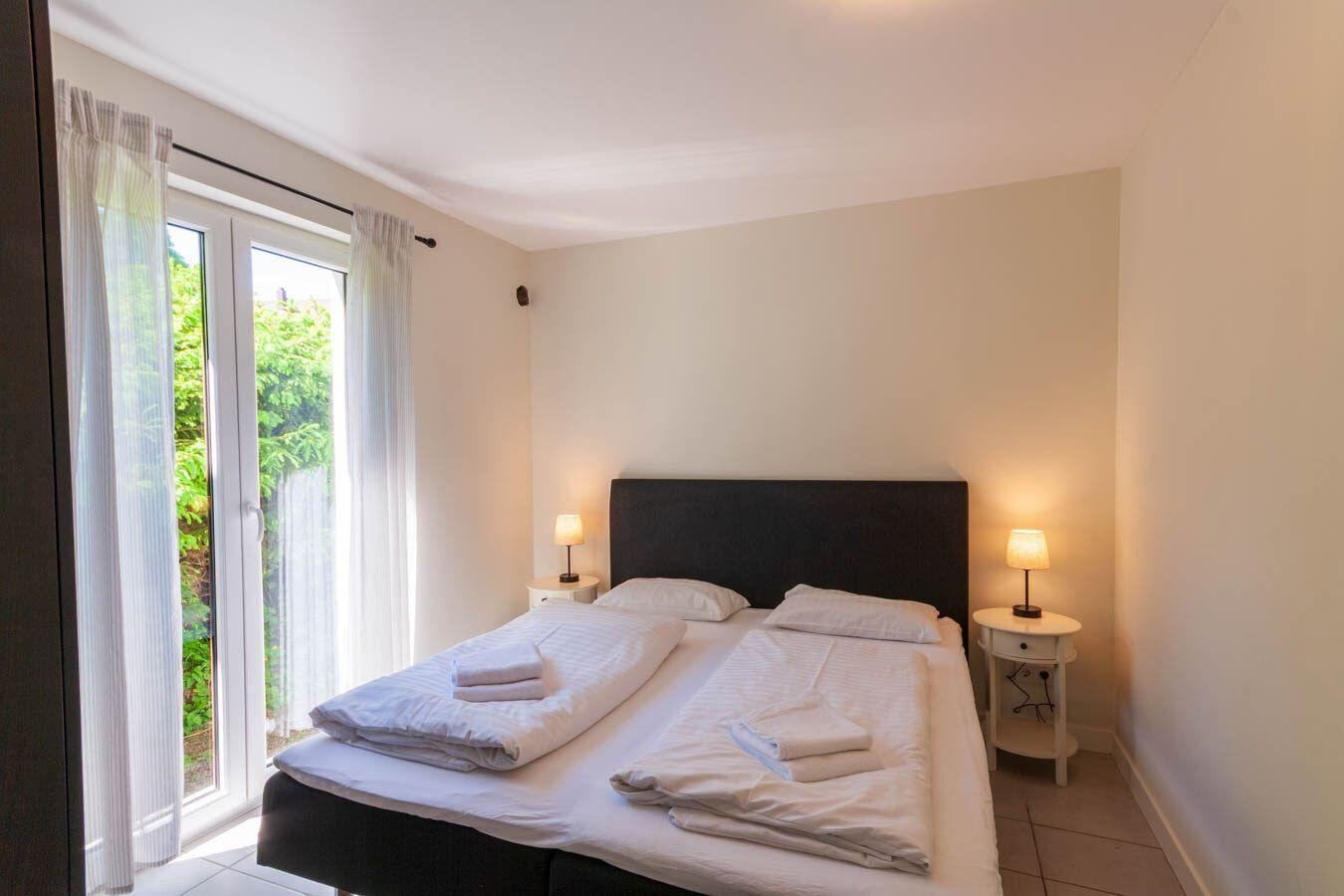 Schlafzimmer mit Doppelbett, zwei Nachttischen und Glastür zum Garten.