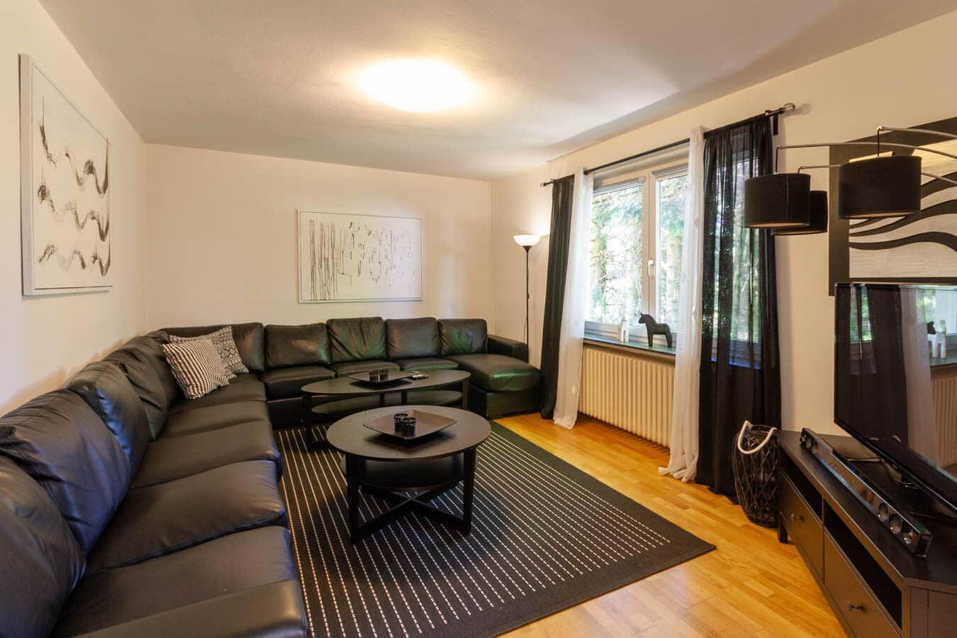 Wohnzimmer mit L-förmigem Sofa, zwei runden Tischen und Fenster mit Blick ins Grüne.
