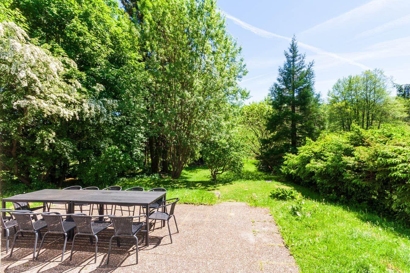 Außenbereich mit Tisch und Stühlen im Grün. Wald und Wiesen umgeben den Platz.