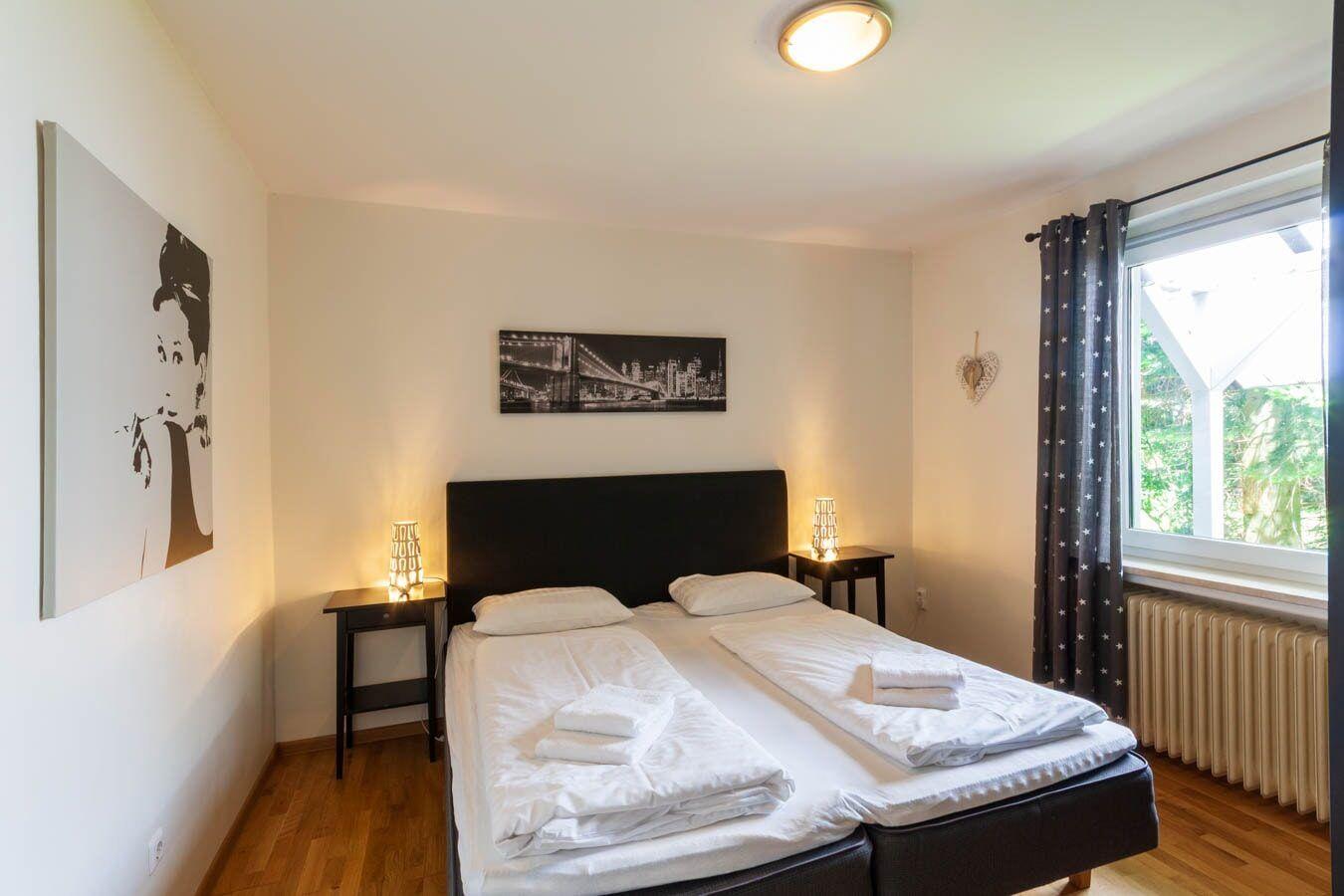 Schlafzimmer mit Doppelbett, zwei Nachttischen und Fenster mit Vorhängen.