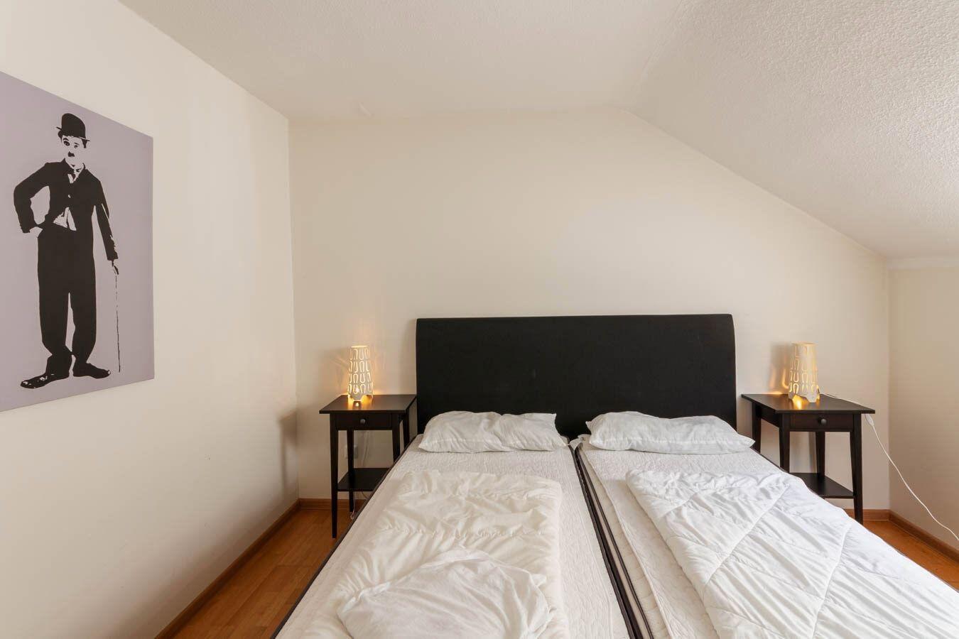 Zimmer mit Doppelbett, zwei Nachttischen und einer Wanddekoration.