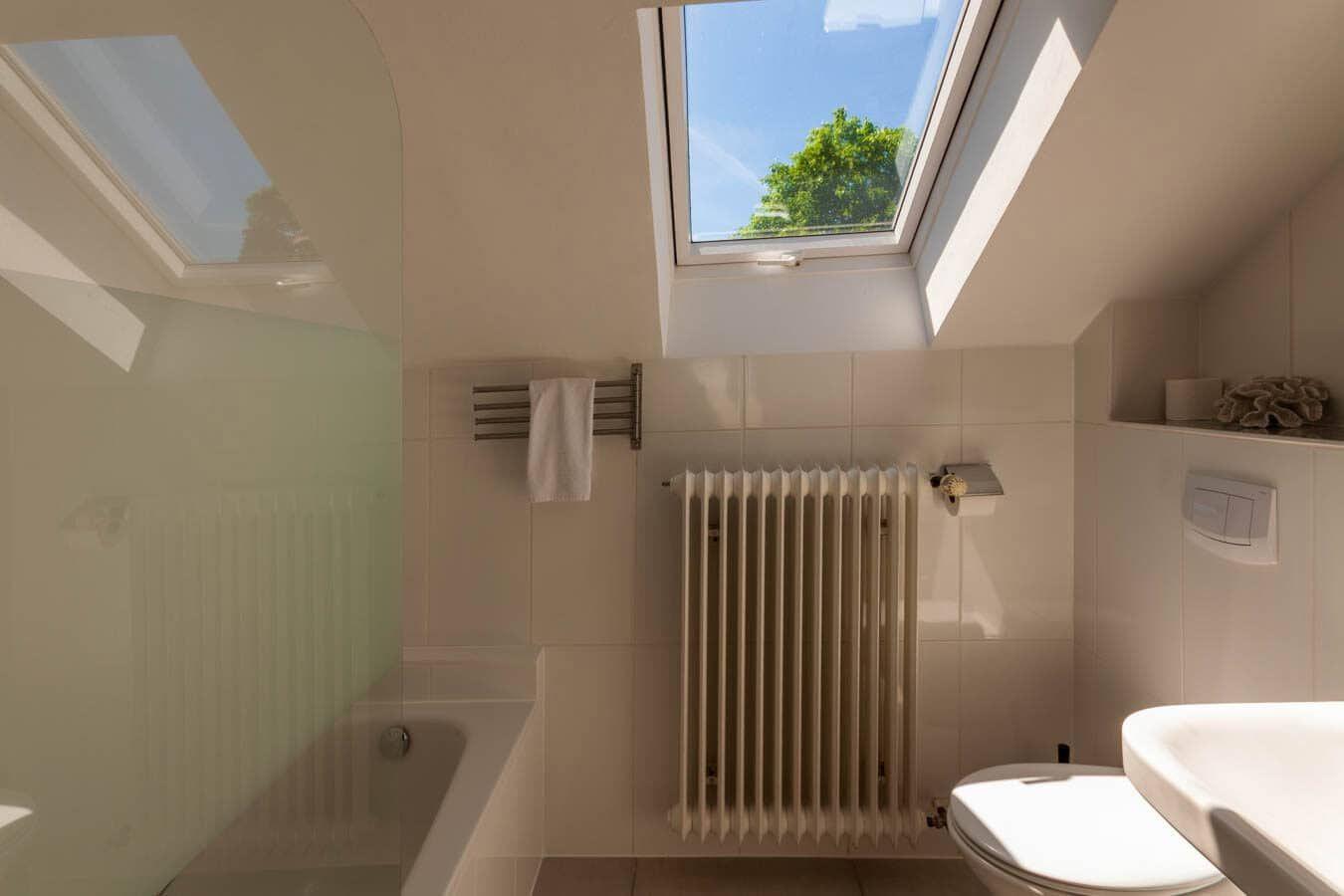 Badezimmer mit Dachfenster, Badewanne, Toilette und Heizkörper.