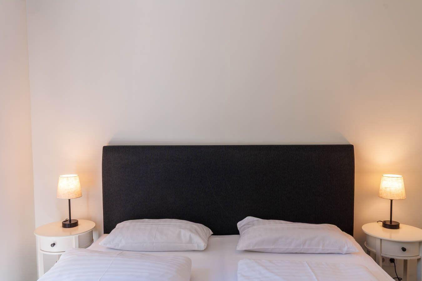 Schlafzimmer mit Bett, zwei Nachttischen und Lampen an den Seiten.