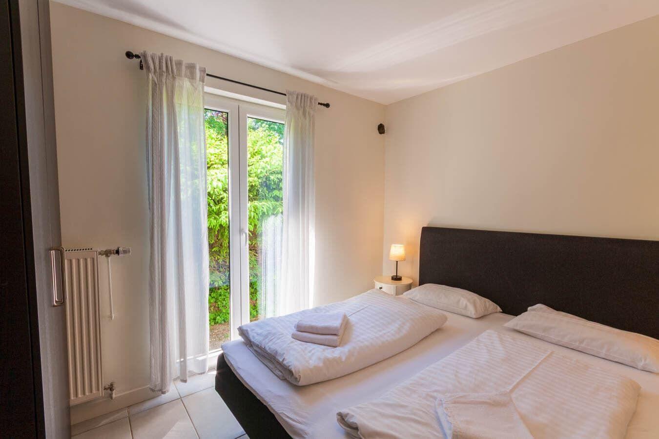 Schlafzimmer mit Bett, Nachttisch und Fenster zur grünen Außenseite.