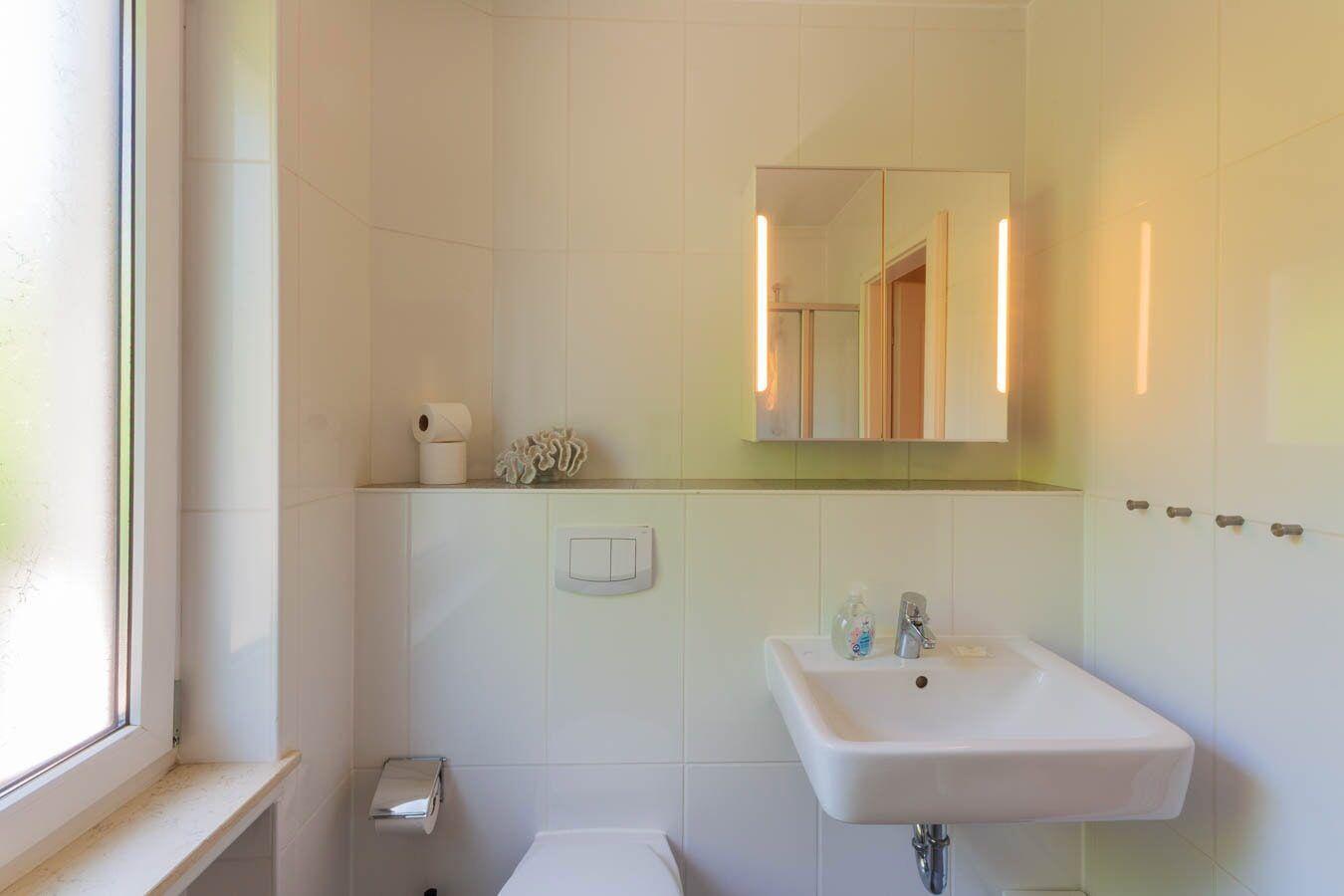 Badezimmer mit Waschbecken, Spiegel und Fenster. Toilettenpapier und Seife sind vorhanden.