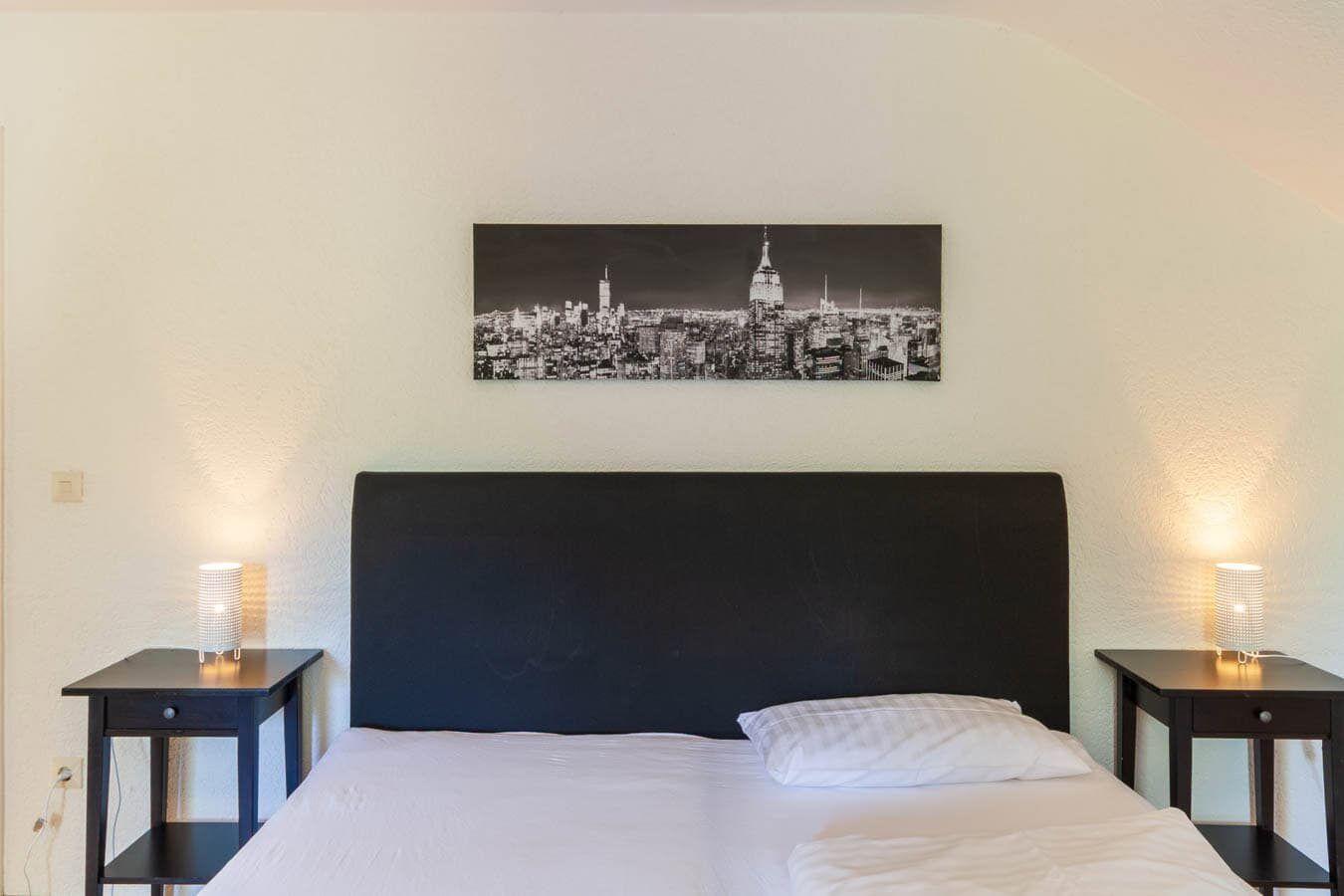 Schlafzimmer mit Bett, Nachttischen und Wandbild von New York