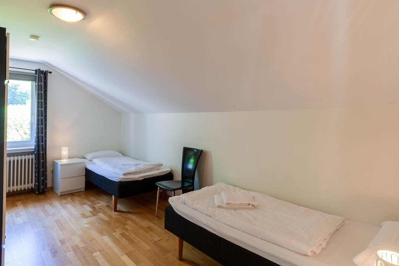 Zwei Betten mit weißen Bettwäschen, Holzboden und schräger Decke.
