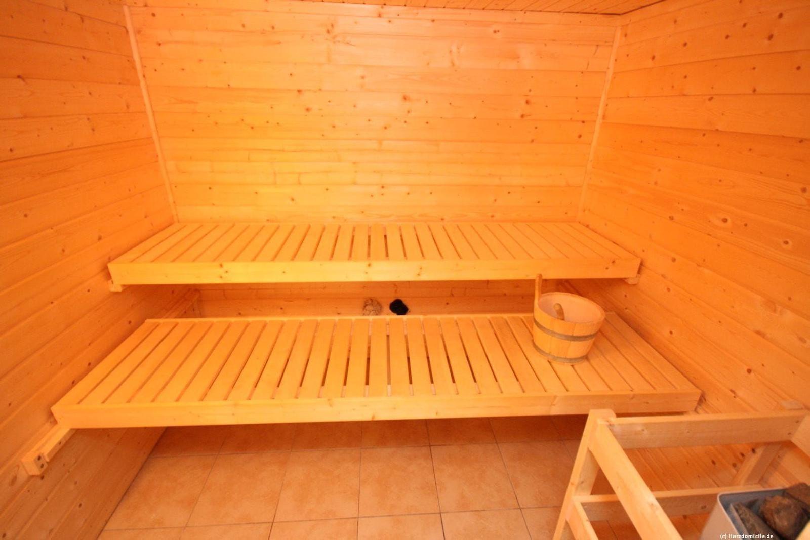 Sauna mit Holzbanken und Eimer. Bodenfliesen und Holzwände.