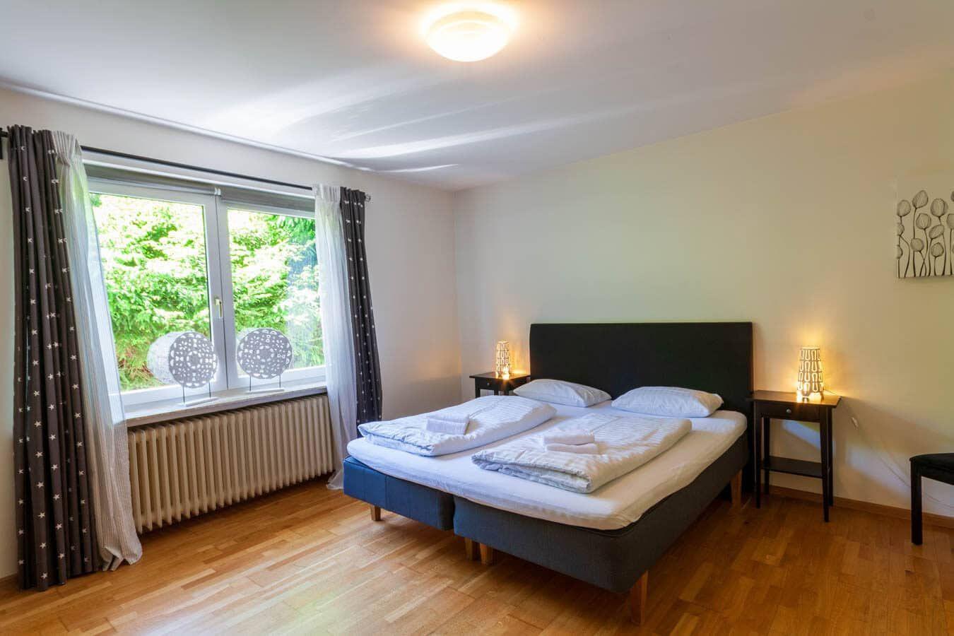 Schlafzimmer mit Doppelbett, Fenster mit Blick auf Grün, Holzboden und zwei Nachttische.